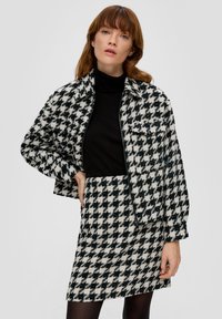 Houndstooth-mustriga lühike jakk ja sobiv seelik mustas ja valges, tekstuuriga viimistlusega ning eest taskud jakil.