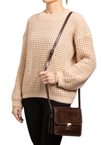 Borsa a tracolla in pelle marrone con chiusura a scatto, forma rettangolare e dettagli cuciti. Maglione intrecciato beige chiaro e pantaloni neri indossati.