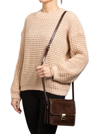 Borsa a tracolla in pelle marrone con chiusura a scatto, forma rettangolare e dettagli cuciti. Maglione intrecciato beige chiaro e pantaloni neri indossati.