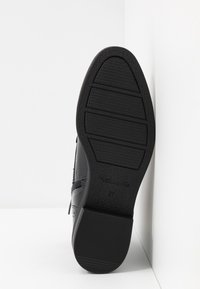 Semelle de chaussure noire avec un motif texturé, dotée d'un léger talon et d'une marque. Panneau latéral lisse avec un détail de fermeture éclair, taille indiquée comme 37.