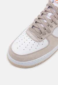 Sneaker grigio chiaro in suede e pelle bianca, con punta forata, lacci piatti e suola in gomma con texture antiscivolo.