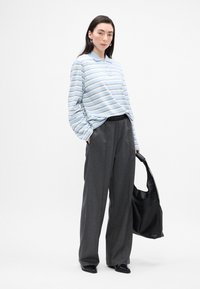 Lyseblå langærmet polo med striber, grå brede bukser og en sort taske. Har subtile mønstre, oversized pasform og tekstureret stof.
