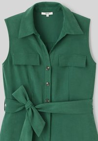 Robe sans manches verte avec un col, deux poches avant, une fermeture à boutons et une ceinture à nouer à la taille. Fabriquée dans un tissu lisse.