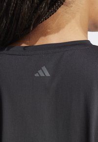 Top atlético negro con texturizado acanalado que presenta un escote redondo y un sutil detalle de logo reflectante en la parte posterior. Textura suave con un diseño ajustado.