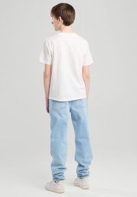 Valkoinen puuvillapaita, lyhyet hihat, yhdistetty vaaleansinisiin farkkuihin. Rentoa istuvuutta, käännetyt hihansuut ja minimalistinen muotoilu.