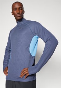 Pull en polaire bleu foncé avec des panneaux latéraux bleu clair, col zippé et manches longues. Présente un tissu texturé et un design ajusté.