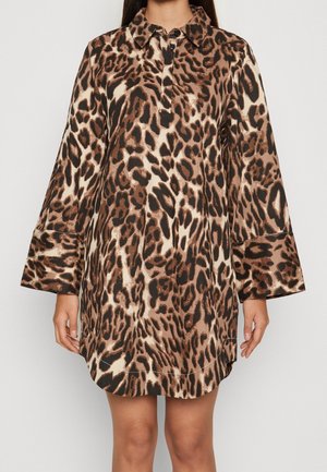 Frau trägt ein knielanges, langärmliges Kleid mit braun-beigem-schwarzem abstraktem Leopardenmuster und kleinem Kragen mit Knopfverschluss.