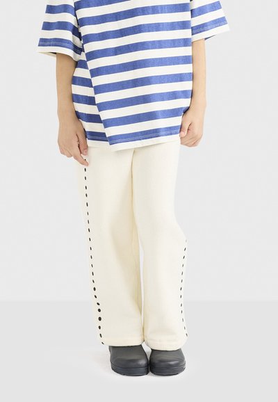 Stribet blå og hvid oversized T-shirt, parret med cremefarvede bukser med sort side-syning. Sorte sko fuldender outfittet.