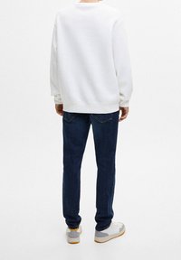 Sudadera blanca de corte relajado, jeans de mezclilla azul y zapatillas gris-blanco. La tela parece suave; el diseño es clásico y casual.