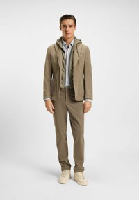 Completo beige a due pezzi con una felpa con cappuccio verde chiaro indossata sotto, abbinata a una camicia a righe azzurro chiaro e sneaker beige.