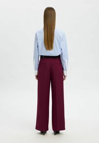 Hellblau gestreifte langärmlige Bluse kombiniert mit burgunderfarbenen, weit geschnittenen Hosen. Ein schwarzer Gürtel und elegante schwarze High Heels runden das Outfit ab.