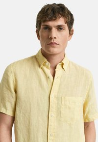 Kurzarmpullover aus gelbem Leinen mit Button-Down-Kragen, einer Brusttasche und einem strukturierten Stoff in lockerer Passform.