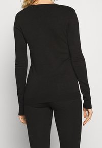 Musta pitkähihainen yläosa, joka on valmistettu pehmeästä materiaalista. Siinä on vartalonmyötäinen leikkaus, pyöreä pääntie sekä resorit hihansuissa ja helmassa.