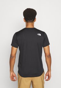 Černé krátké sportovní tričko s kulatým výstřihem, s bílým logem na horní části zad. Vyrobeno z hladkého, lehkého materiálu.