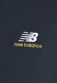 Tessuto nero con una texture liscia presenta un logo ricamato bianco "NB" con accenti di movimento e "new balance" in giallo sottostante.