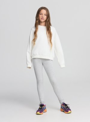 Felpa oversize bianca, leggings grigi e sneakers sportive multicolori. Tessuti lisci con una vestibilità comoda e dettagli minimalisti.