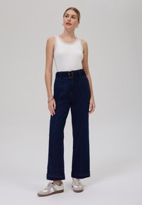 Högmidjade, marinblå denimbyxor med vida ben, detaljerad sömnad och ett bälte med en rektangulär spänne; matchat med en vit linne och sneakers.