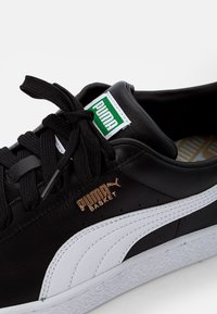 Fekete bőr sneaker fehér kiegészítőkkel, lekerekített orral, lapos fűzős kivitelben, arany logó részletezéssel és textúrázott gumi talppal.