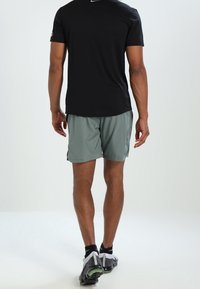 Černé sportovní tričko s krátkým rukávem a šedé lehké šortky. Reflexní detaily na tričku a sportovních botách s textured podrážkami.