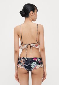 Bikini-Oberteil mit floralen Mustern und gerüschten Kanten, hinten gebunden. Passender Bikini-Slip, blau mit floralem Design und gerüschtem Saum. Weicher Stoff.