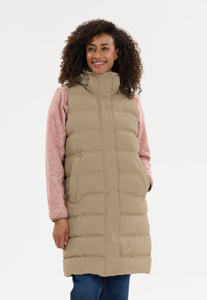 Beige puffer vest med høj krave og trykknaplukning, med sidelommer og quiltet tekstur, lagdelt over en lyserød langærmet top.