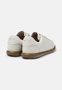 White Camper sneakers with a brown sole, featuring a smooth design and visible logo on the heel, positioned to showcase the back view.