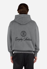 Grijze hoodie van zacht materiaal, met een logo en de tekst "Everyday Ambition" in het zwart op de rug. Oversized design met geribbelde manchetten.