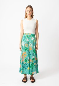 Groene bloemige rok met oranje, roze en witte patronen, gecombineerd met een geribde witte mouwloze top en bruine sandalen met banden.