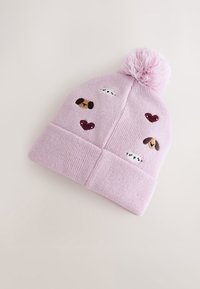 Bonnet rose tricoté avec un pompon sur le dessus, présentant des visages de chiens brodés et des cœurs de différentes couleurs sur le corps. Texture douce.