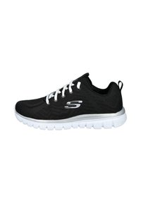 Zapatilla deportiva negra con parte superior de malla, cordones blancos y suela blanca. Presenta un logo en el costado y tela texturizada para transpirabilidad.