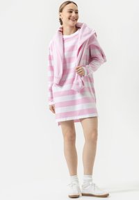 Roze en witte gestreepte langemouwen jurk met een ronde hals, met een witte sweatshirt over de schouders en casual sneakers.