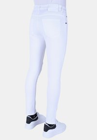 Witte skinny jeans met een gladde textuur, voorzien van achterzakken en een hoge taille, gecombineerd met witte sneakers met zwarte accenten.