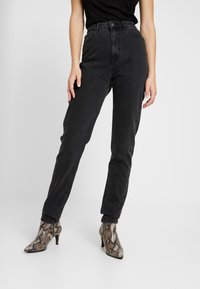Jeans negros de cintura alta con un acabado texturizado, que cuentan con un cierre de botón y cremallera. Combinados con botas de tacón con estampado de piel de serpiente.