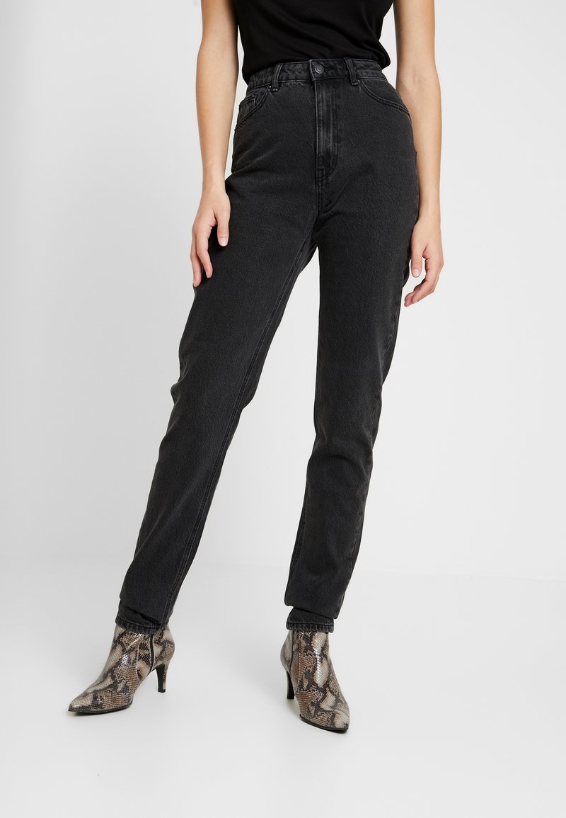 Jeans negros de cintura alta con un acabado texturizado, que cuentan con un cierre de botón y cremallera. Combinados con botas de tacón con estampado de piel de serpiente.