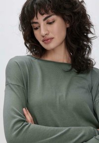 Haut à manches longues, coupe décontractée en tissu vert doux. Texture douce avec un col large et des épaules tombantes, doté d'une légère maille côtelée.