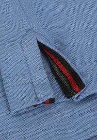Helles blaues Poloshirt-Gewebe mit einer strukturierten Webart; hat einen kontrastierenden Innenbereich in Schwarz und Rot am Saum, mit genähten Details.