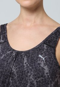 Svart linne med ett geometriskt mönster i grå nyanser, tillverkat av elastiskt tyg, med en diskret logotyp på vänster sida.