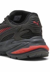 Scarpa da atletica nera con tomaia sintetica texturizzata, dettagli rossi, suola ammortizzata e un design curvo distintivo per il supporto.