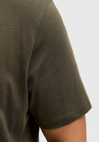 T-shirt z krótkim rękawem w oliwkowym kolorze z gładką fakturą i wzmocnionymi szwami na rękawach, prezentowany na neutralnym tle.