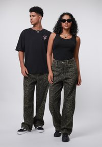 Leopard print cargo pants in olive green, paired with a black tank top and oversized black t-shirt. Accessories include sunglasses and necklaces.