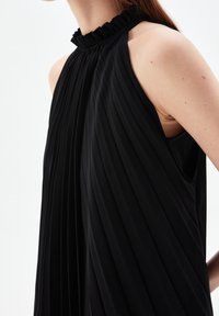 Svart ärmlös klänning med vertikala veck, en ruffled hög halsringning och en lös passform, tillverkad av ett smidigt tyg med en mjuk textur.