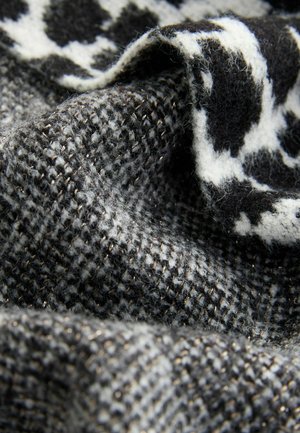 Audiniu su tekstūra, kuriame yra juodai baltas raštas su houndstooth dizainu, praskiedžiamu metaliniais siūlais akcentui.