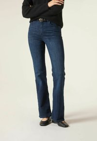 Pantalones de mezclilla de campana azul oscuro con una cintura de media altura, confeccionados en una tela suave. Presentan un diseño clásico de cinco bolsillos y trabillas para cinturón.