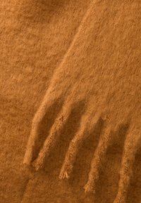 Scarf in lana color tan con una superficie morbida e texturizzata, con dettagli di frange a un'estremità. Il tessuto ha un aspetto caldo e soffice.