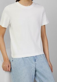 Biała bawełniana koszulka z krótkim rękawem, z okrągłym dekoltem i luźnym krojem. Do tego jasnoniebieskie dżinsy.