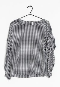Blouse à manches longues à carreaux noir et blanc avec un col arrondi, des détails de manches volantées et une petite ouverture en forme de trou de serrure à l'arrière.