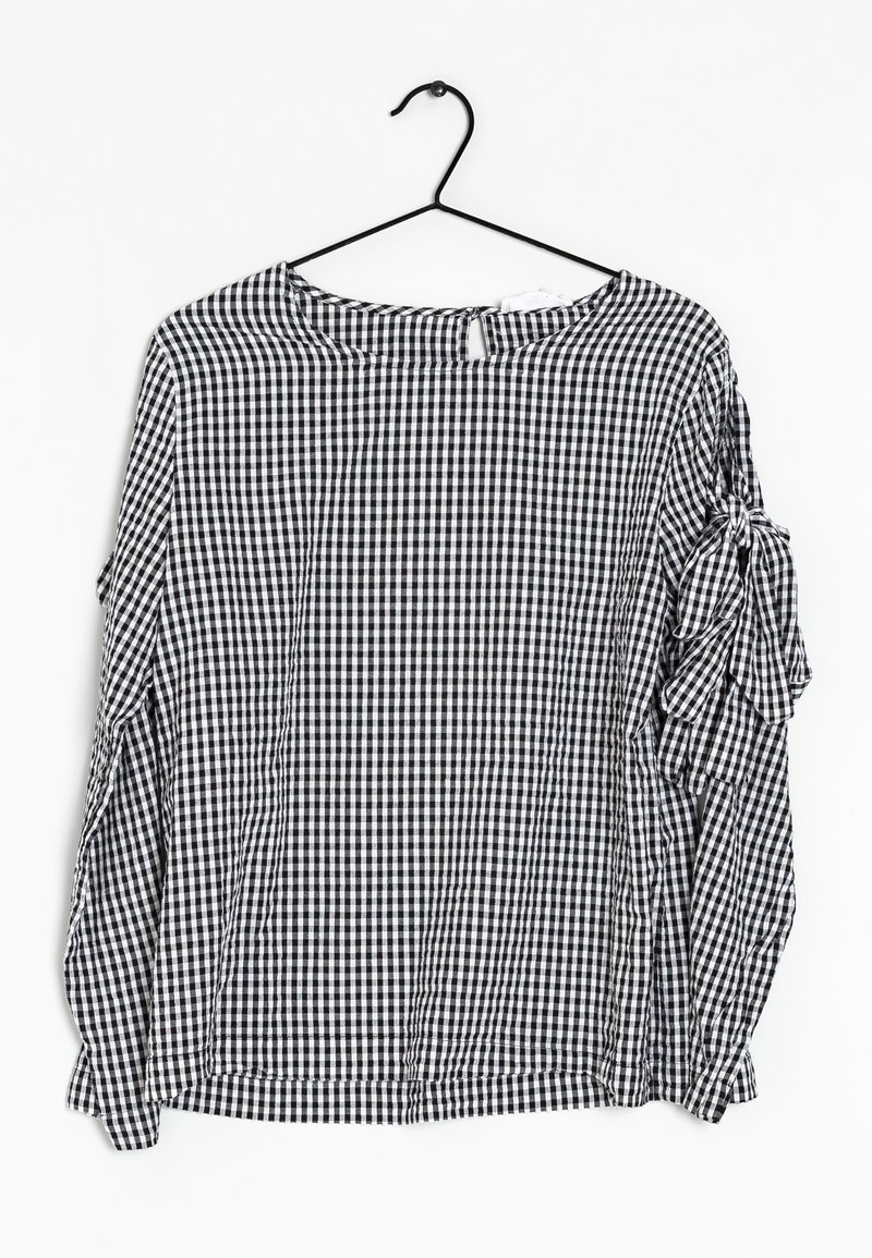 Blouse à manches longues à carreaux noir et blanc avec un col arrondi, des détails de manches volantées et une petite ouverture en forme de trou de serrure à l'arrière.