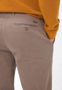 Pantalon en coton couleur beige avec une coupe slim. Dispose d'une poche arrière avec une fermeture à bouton et d'un petit accent en métal de marque.