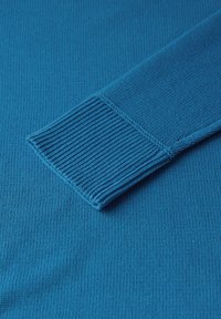 Sininen neulepusero, jossa on ribbireunus, esittelee läheltä käsivarren tekstuuria ja yksityiskohtia samansävyisellä kankaalla.