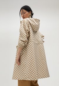 Beżowa wodoodporna kurtka z powtarzającym się geometrycznym wzorem, z kapturem, elastycznymi mankietami i bocznymi kieszeniami dla większej funkcjonalności.